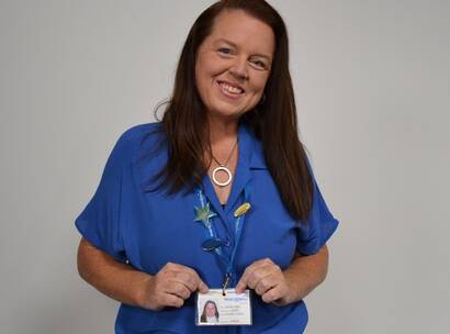 Louise smiling to camera in a blue top and holding her make-a-wish volunteer ID card