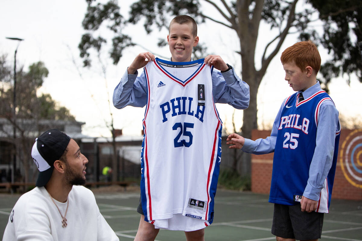 Make-A-Wish Australia wish kid Charlie holding up Philadelphia 76ers basketball top with basketball star Ben Simmons and his brother