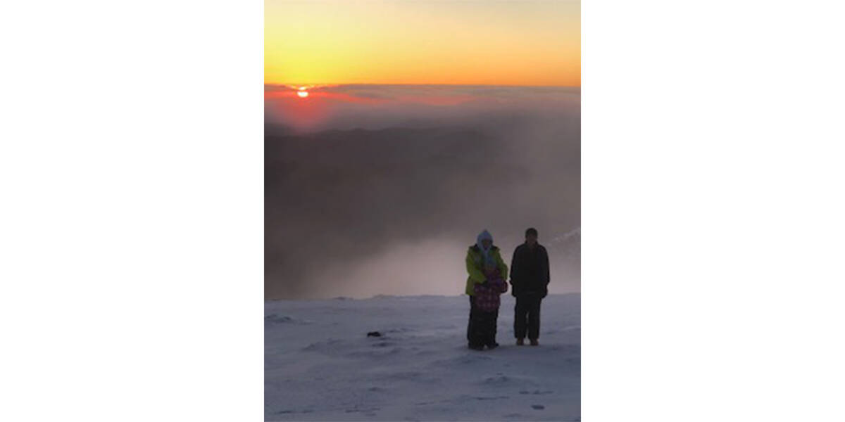 Harry and his family stand on a snowy hilltop with an orange sun setting behind them