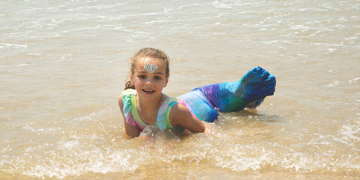 Make-A-Wish kid Jazmyn smuiles dresses as a mermaid in shallow water on the beach