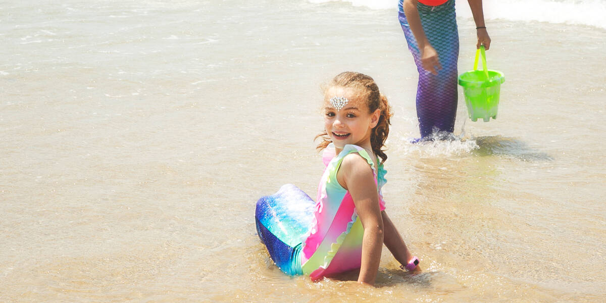Make-A-Wish kid Jazmyn dressed as mermaid on a beach turns to face the camera
