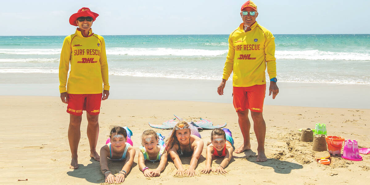 Make-A-wish kid Jazmyn with her sisters and a mermaid on a beach with two lifeguards
