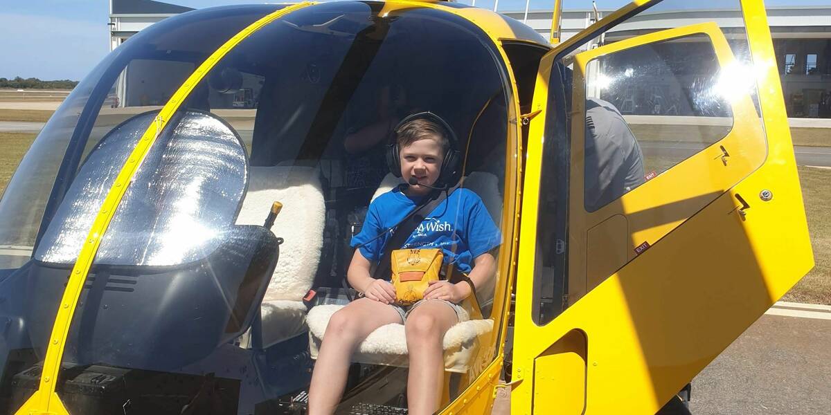 Make-A-Wish kid Henry sits in the front of a yellow helicopter on his wish day